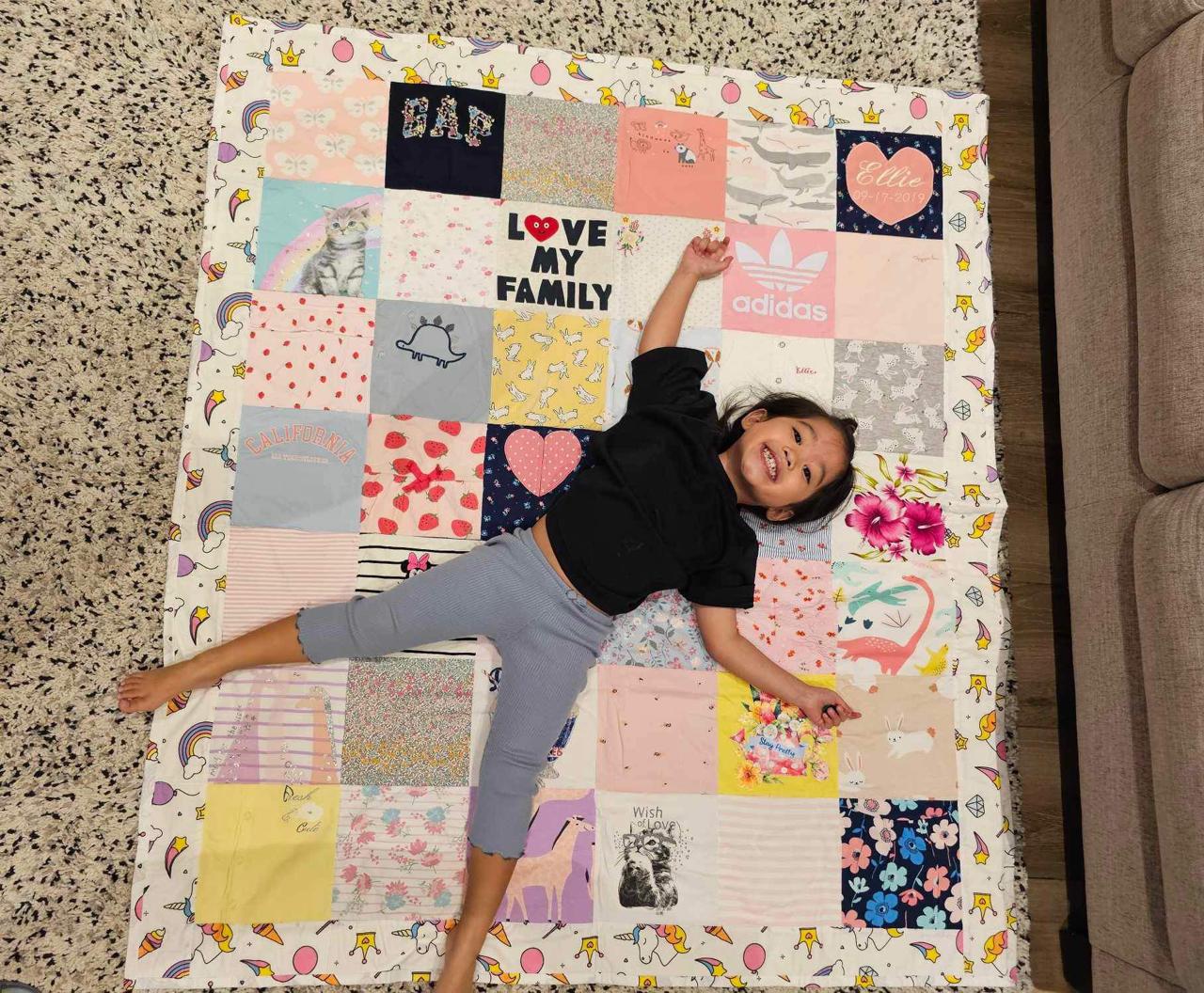 A child smiling on a colourful handmade memory quilt made from cherished clothes
