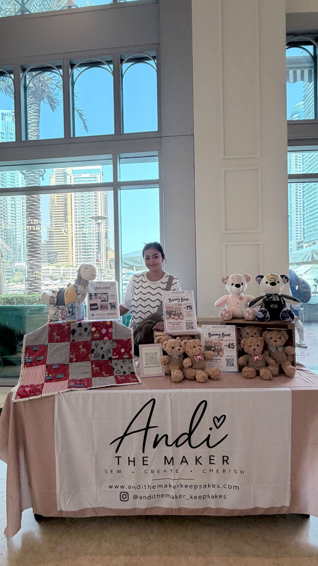 Andi behind her branded table displaying a memory quilt, camels, memory bears and Benny Bears
